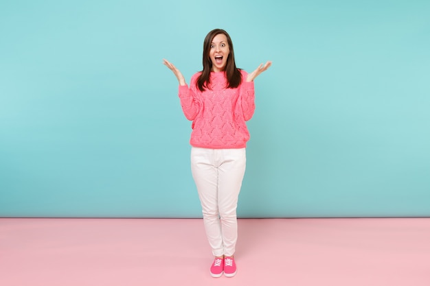 Portrait de toute la longueur d'une jeune femme souriante en pull rose tricoté, pantalon blanc posant