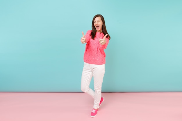 Portrait de toute la longueur d'une jeune femme souriante en pull rose tricoté, pantalon blanc posant