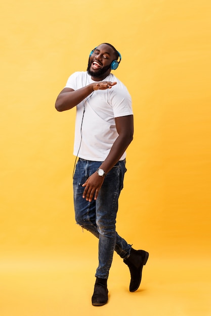 Photo portrait de toute la longueur d'un jeune homme afro-américain, cerise, écouter de la musique avec des écouteurs