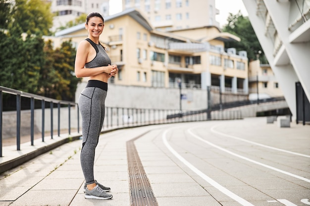 Portrait de toute la longueur d'une jolie femme athlétique souriante en tenue allant s'entraîner dans le centre-ville