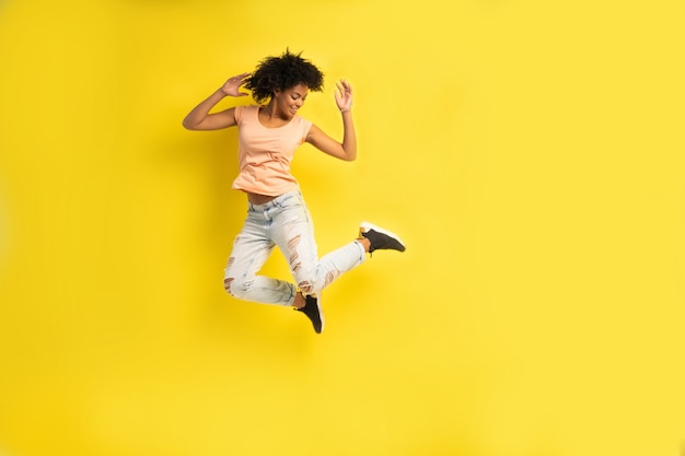Portrait de toute la longueur d'une joyeuse jeune femme africaine célébrant le succès en sautant isolé sur fond jaune.