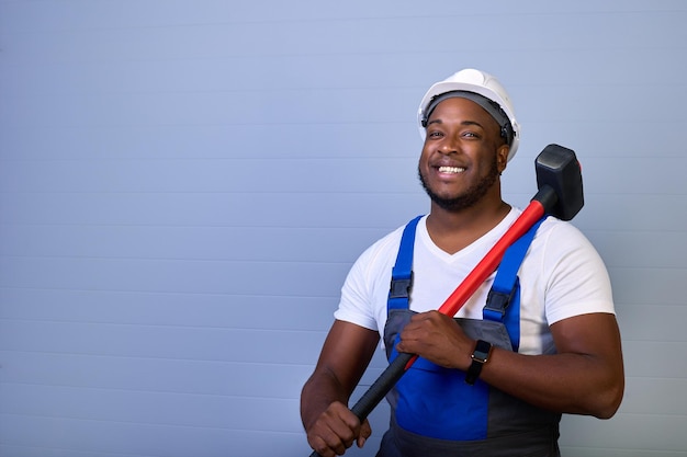 Portrait d'un travailleur afro-américain heureux en salopette avec un marteau dans les mains