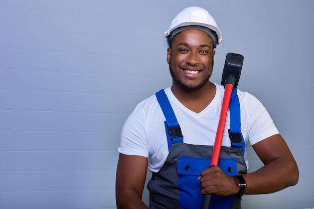 Portrait d'un travailleur afro-américain heureux en salopette avec un marteau dans les mains