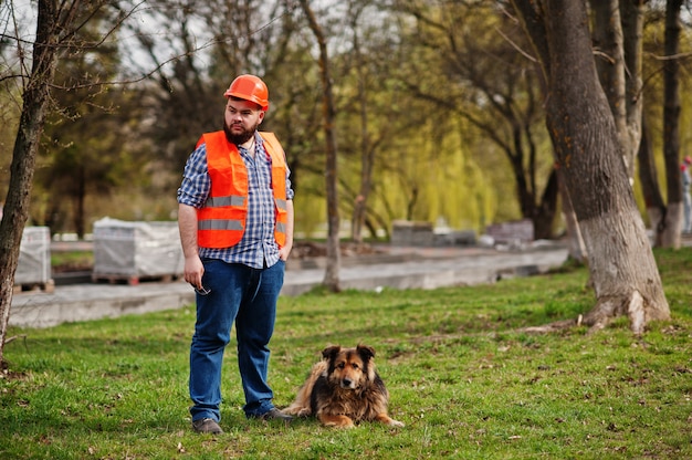 Portrait de travailleur de la barbe brutal homme costume ouvrier dans un casque orange de sécurité avec chien de garde.