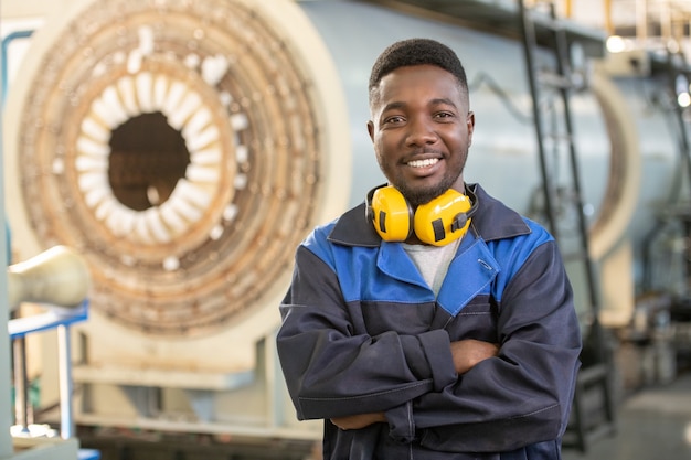 Photo portrait d'un travailleur de la fabrication barbu sérieux dans un casque et une salopette mettant des gants de travail de sécurité tout en se préparant à la ferronnerie