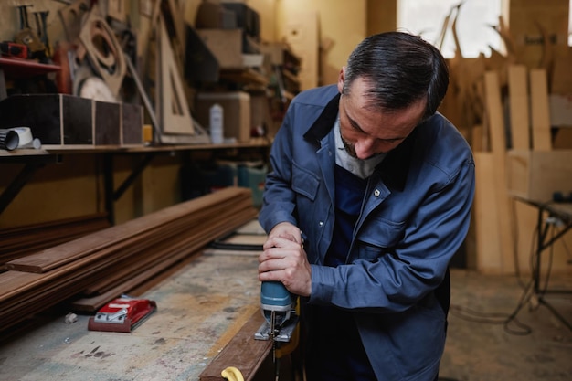 Portrait d'un travailleur masculin mature coupant du bois dans un atelier d'usine avec un espace de copie d'outil électrique