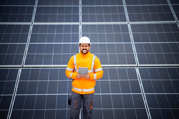 Portrait d'un travailleur professionnel debout près de panneaux solaires et vérifiant la production d'énergie
