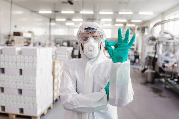 Portrait de travailleur en uniforme de protection avec des gants en caoutchouc debout dans l'entrepôt et montrant un signe correct avec la main. Concept d'épidémie de virus Corona.