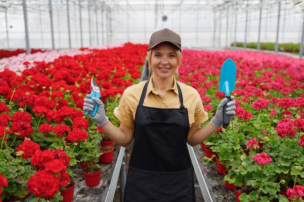 Portrait d'une travailleuse de serre joyeuse avec un outil de jardinage dans les mains