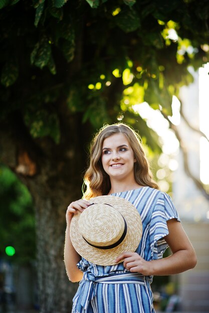 Portrait d'une très jolie jeune femme en combinaison rayée posant avec son chapeau sur un trottoir en ville