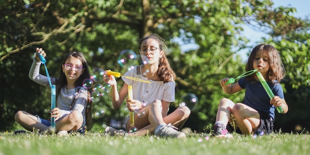 Portrait de trois belles sœurs caucasiennes soufflant des bulles de savon alors qu'elles sont assises dans le parc