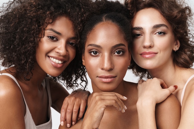 Portrait de trois femmes multiraciales brunes se tenant ensemble et regardant la caméra