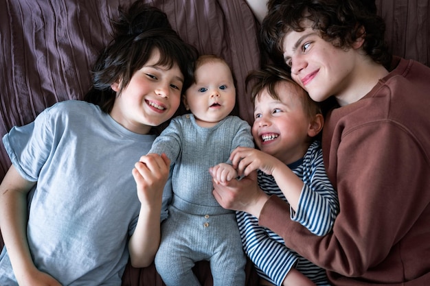 Portrait de trois frères allongés sur le lit avec leur bébé frère et sœur enfants positifs d'âges différents grand concept de famille heureux ensemble