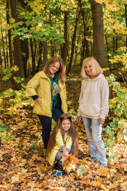 Portrait de trois générations de belles femmes heureuses et chien regardant la caméra, étreignant et souriant dans la nature automnale.