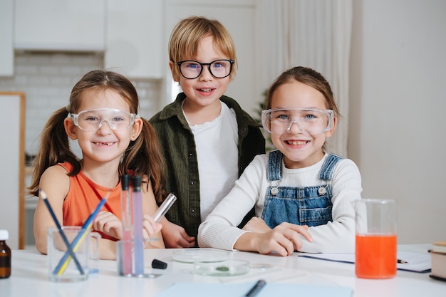 Portrait de trois petits enfants heureux faisant un projet de science à domicile, tous derrière une table.