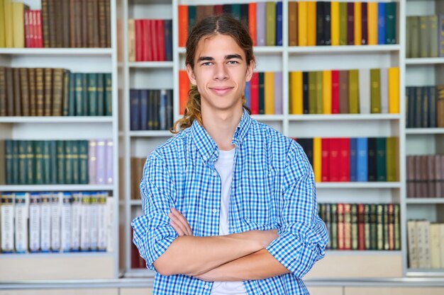 Portrait unique d'un adolescent étudiant souriant et confiant regardant la caméra dans la bibliothèque