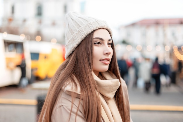 Portrait urbain d'une belle jeune fille dans un bonnet tricoté à la mode avec une veste d'hiver se promène dans la ville à la foire