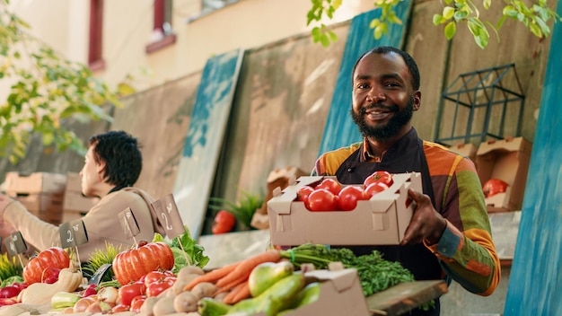 Photo portrait d'un vendeur vendant une boîte remplie de tomates bio et faisant la publicité de ses propres produits locaux sur le marché des agriculteurs locaux. propriétaire d'une petite entreprise d'agriculteur masculin à la foire alimentaire. prise de vue à main levée.