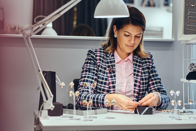 Portrait d'une vendeuse élégamment vêtue emballant de précieuses boucles d'oreilles dans une boîte pour son client dans une bijouterie de luxe.