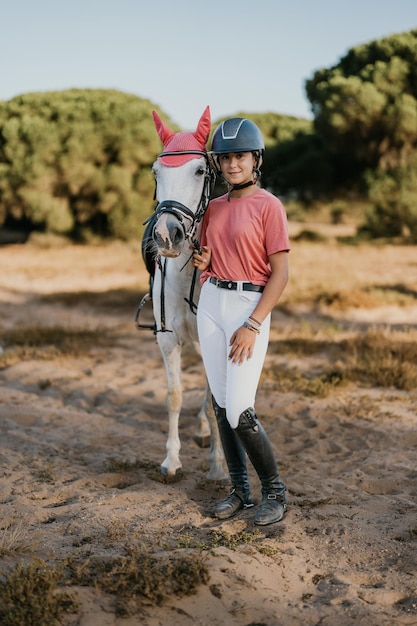 Portrait vertical d'une adolescente debout en robe rose avec son cheval blanc