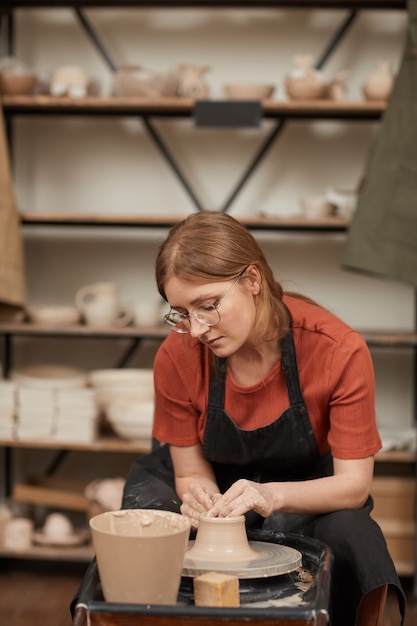 Portrait vertical aux tons chauds d'une jeune femme façonnant de l'argile sur un tour de poterie en atelier tout en profitant des arts et de l'artisanat, espace de copie