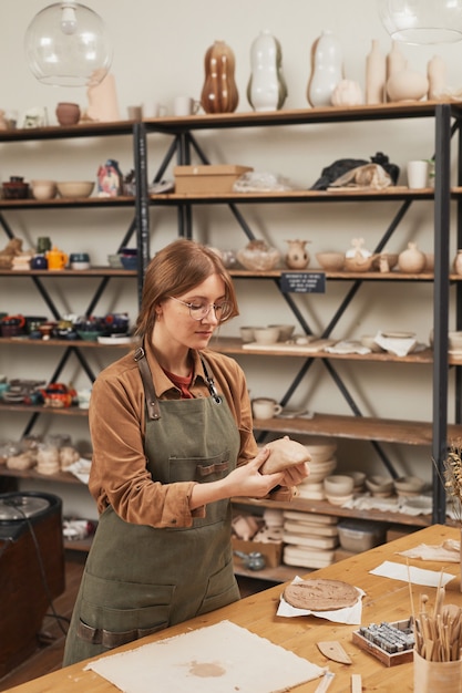 Portrait vertical aux tons chauds d'une jeune femme façonnant l'argile tout en fabriquant de la céramique dans un atelier de poterie, concept de petite entreprise, espace de copie