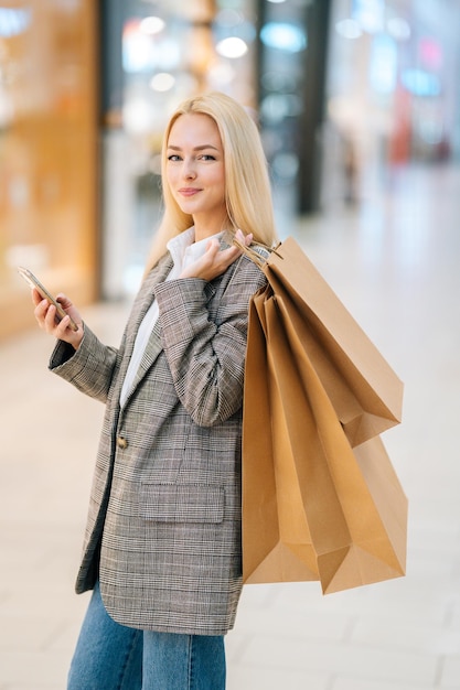 Portrait vertical d'une charmante jeune femme blonde élégante en manteau élégant regardant la caméra tenant