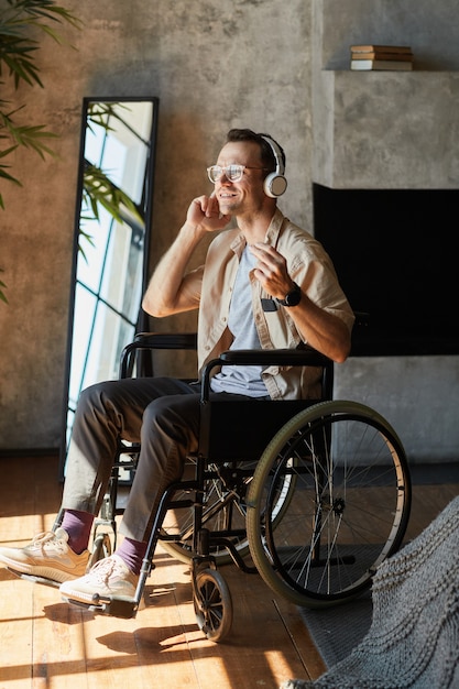 Portrait vertical complet d'un homme handicapé moderne en fauteuil roulant, profitant de la musique à la maison