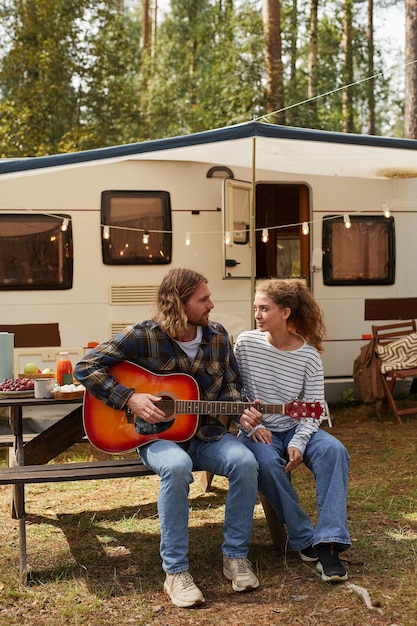 Portrait vertical complet d'un jeune couple heureux jouant de la guitare tout en profitant du camping en plein air avec ...