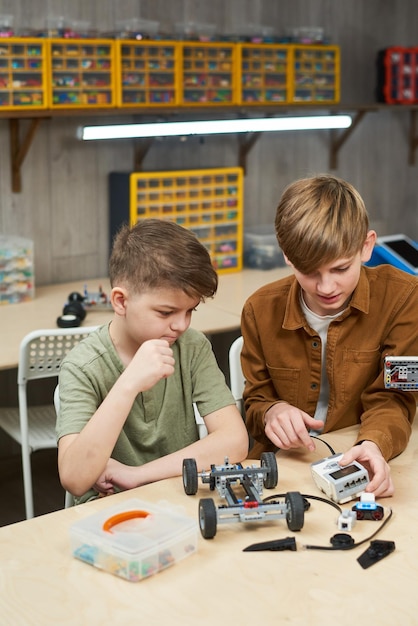 Portrait vertical de deux garçons assemblant une voiture électrique profitant d'un cours de robotique à l'école