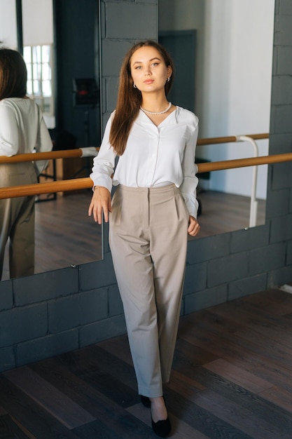 Portrait vertical de l'élégance confiante jeune femme portant des vêtements élégants regardant la caméra debout dans la chambre avec miroir Enseignante assez réussie posant dans la classe d'art