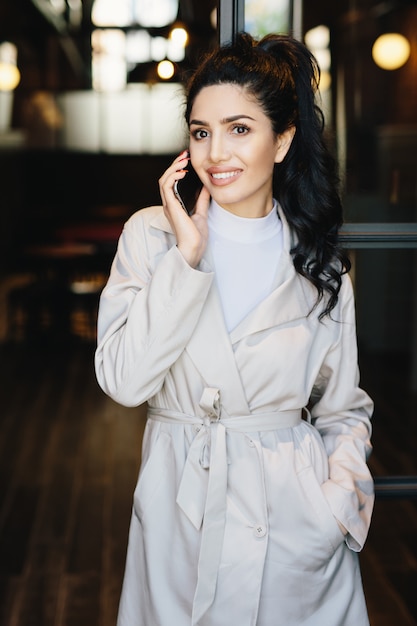 Portrait Vertical D'élégante Femme Brune En Blouse Blanche, Communiquant Par Téléphone Portable