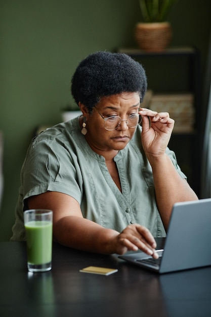 Portrait vertical d'une femme âgée noire utilisant un ordinateur portable et faisant des achats en ligne depuis la maison