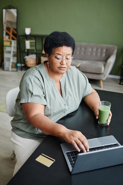 Portrait vertical d'une femme âgée noire utilisant un ordinateur portable à la maison et faisant des achats en ligne ou payant des impôts