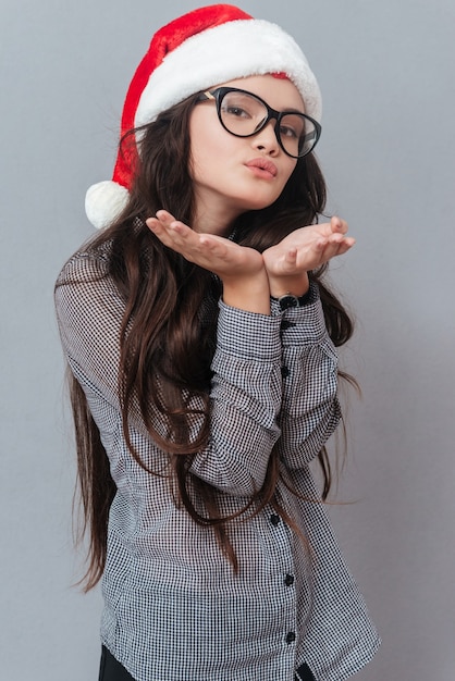 Portrait vertical d'une femme asiatique dans un baiser d'air de sables de chapeau de noël isolé sur fond gris