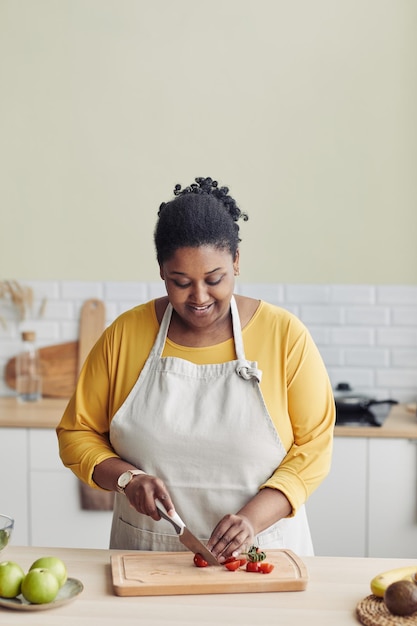 Photo portrait vertical d'une femme noire souriante préparant un repas sain dans la cuisine et coupant des légumes