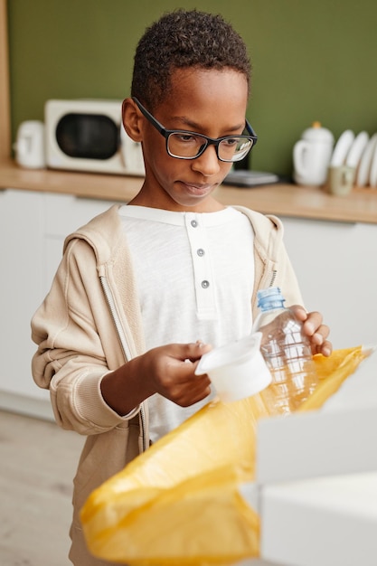 Portrait vertical d'un garçon afro-américain mettant du plastique dans des bacs de recyclage à la maison