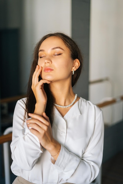 Portrait vertical en gros plan d'une jeune femme confiante portant des vêtements élégants debout dans la chambre avec un miroir touchant les cheveux avec les mains fermées les yeux