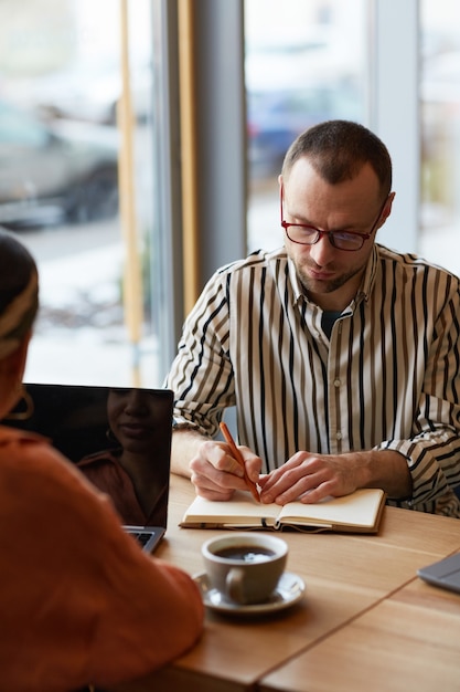 Portrait vertical d'un homme adulte prenant des notes et écrivant lors d'une réunion d'affaires à une table de café