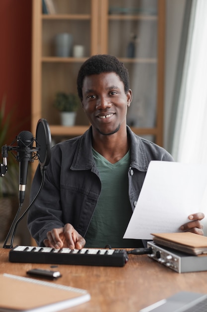 Portrait vertical de l'homme afro-américain souriant chantant au microphone tout en enregistrant de la musique en home studio