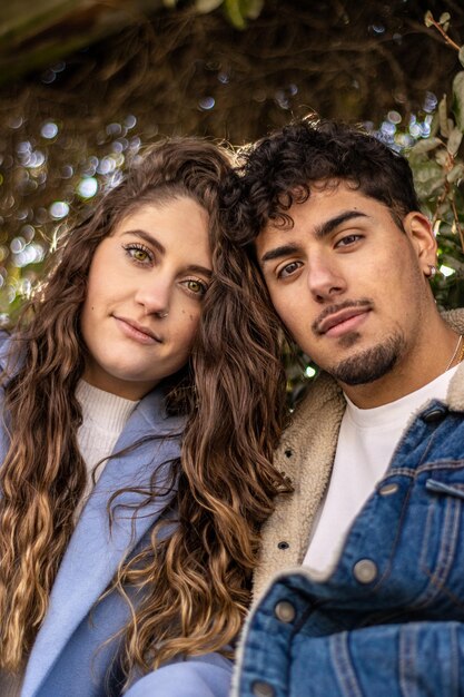 Portrait vertical d'un homme latino et d'un jeune couple de femme caucasienne posant avec leurs têtes ensemble regardant la caméra, nature de fond verticale