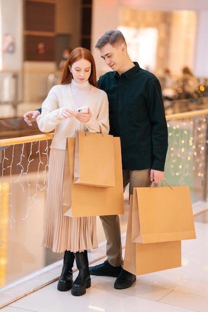 Portrait vertical d'un jeune couple perplexe à la recherche d'un magasin dans l'application de navigation du centre commercial sur