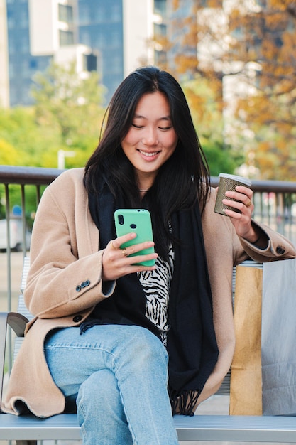 Portrait vertical d'une jeune femme asiatique insouciante tapant un message à l'aide d'un téléphone portable et prenant un