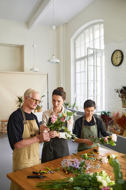 Portrait vertical d'une jeune femme fleuriste enseignant un couple d'âge mûr organisant des compositions florales en atelier