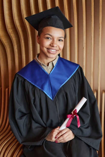 Portrait vertical d'une jeune femme souriante portant une robe de graduation et souriant à la caméra tout en posant à l'intérieur