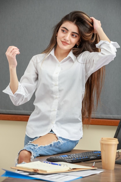 Portrait vertical d'une jeune fille assise au bureau et étirant ses cheveux