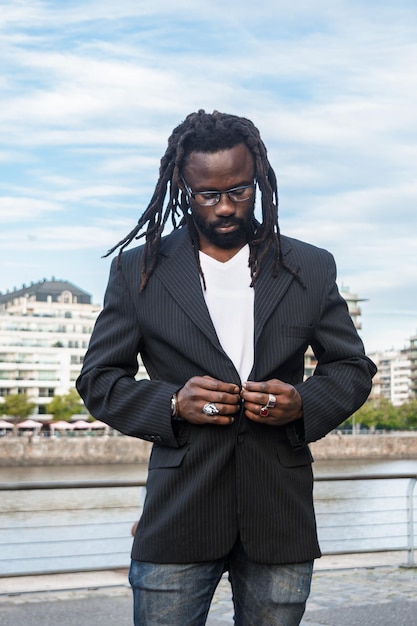 Portrait vertical d'un jeune homme africain à l'extérieur en train de boutonner son blazer