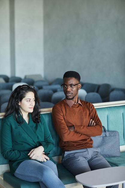 Portrait Vertical De Jeune Homme Afro-américain Assis Avec Une Femme Du Moyen-orient Assis Sur Des Chaises Dans Un Auditorium En Attendant Un Séminaire Ou Une Classe, Copiez L'espace