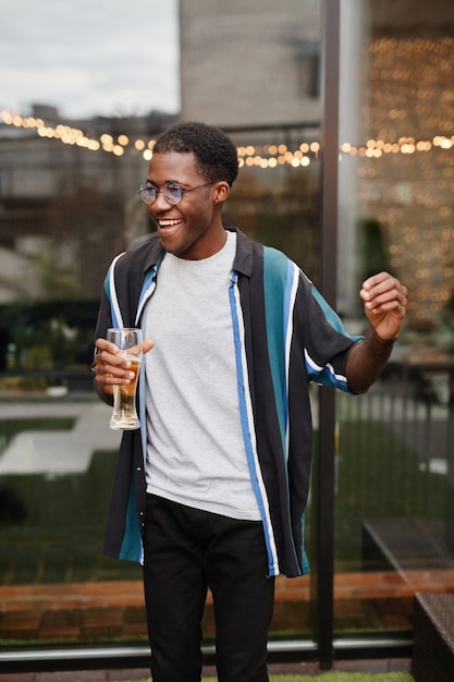 Portrait vertical d'un jeune homme afro-américain tenant un verre tout en profitant d'une fête en plein air sur le toit