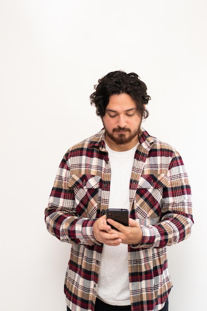 Portrait vertical de jeune homme regardant sérieusement son téléphone portable sur fond blanc